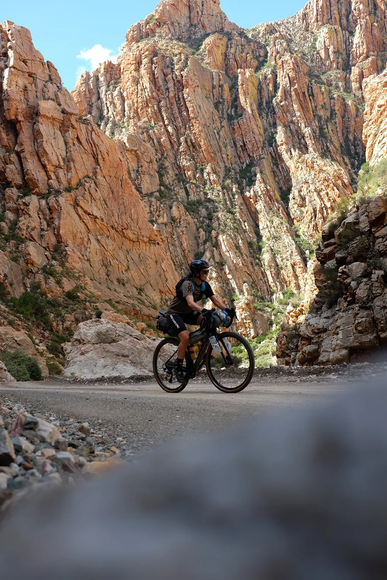 A cyclist climbing the gravel road of the Swartberg Pass, flanked by towering folded rock walls
